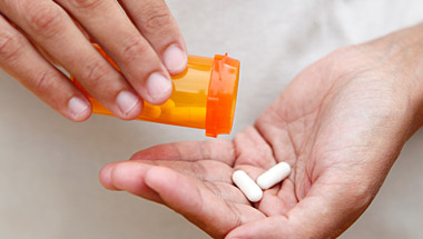 A hand tipping out pills from a pill bottle into an open palm