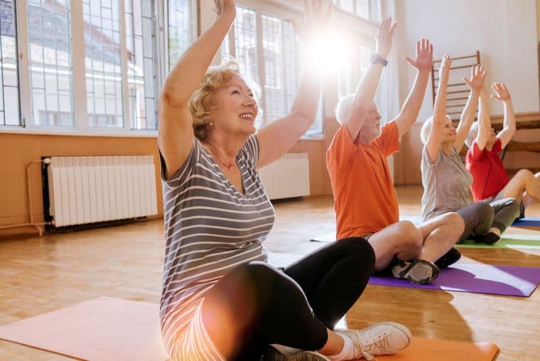Four older people at a yoga class in a sunny gymnasium.
