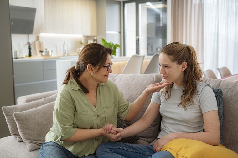 An older woman talking to a teenage girl on a sofa and holding her hand