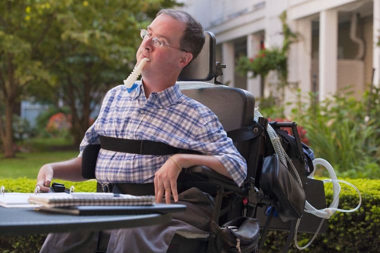 Businessman with Duchenne muscular dystrophy using breathing ventilator doing paperwork at a cafe