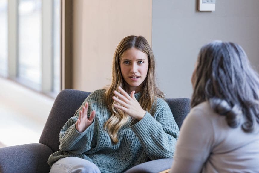 Female university student talking to peer on sofa