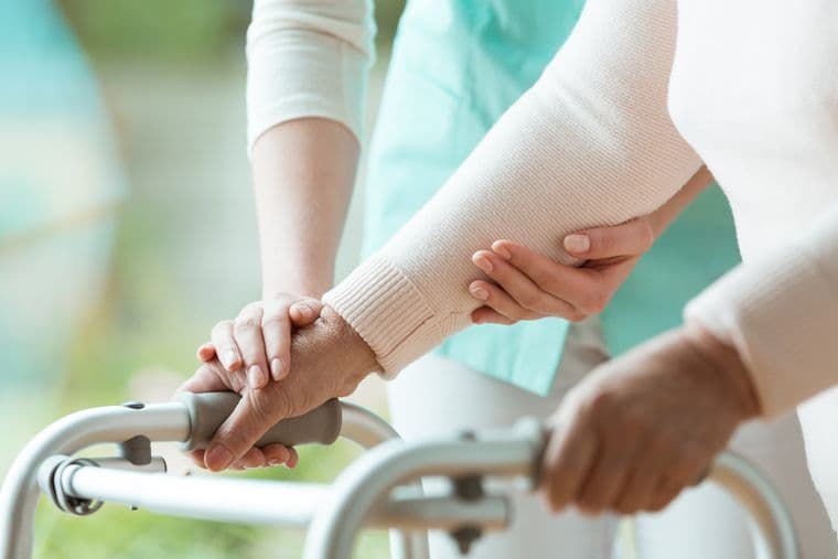 A woman using a walking frame receives help during her rehabilitation