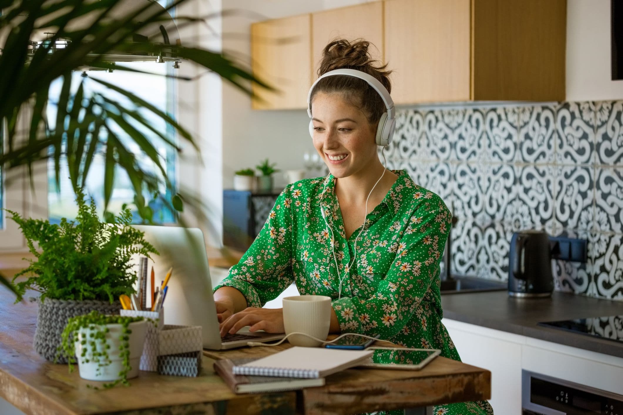 A woman working from home wearing headphones while using a laptop