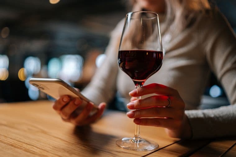 Woman reading phone and holding glass of red wine