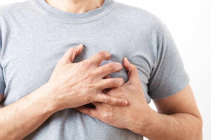 A person wearing a gray shirt is holding their chest with both hands, suggesting chest discomfort or pain.