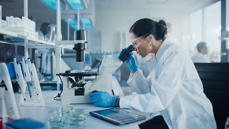 female scientist in a lab using a microscope to analyse a sample on a petri dish