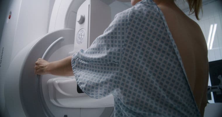 A woman in a hospital gown prepares for a mammogram, adjusting the machine in a medical examination room.