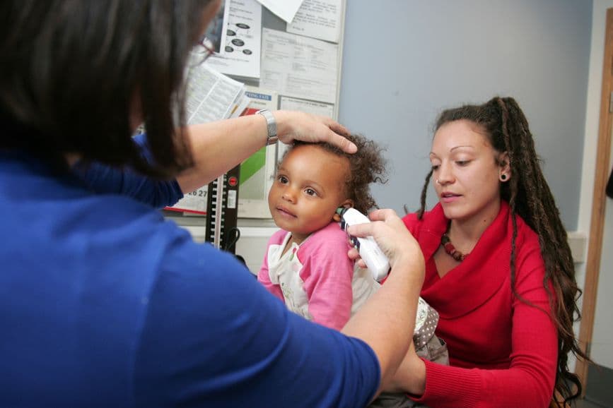 A woman, with her child sat on her lap, in a doctors office.