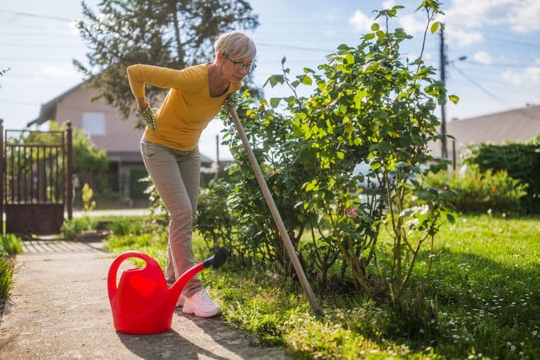 an older woman outside in the garden is holding her back in discomfort as she leans forward