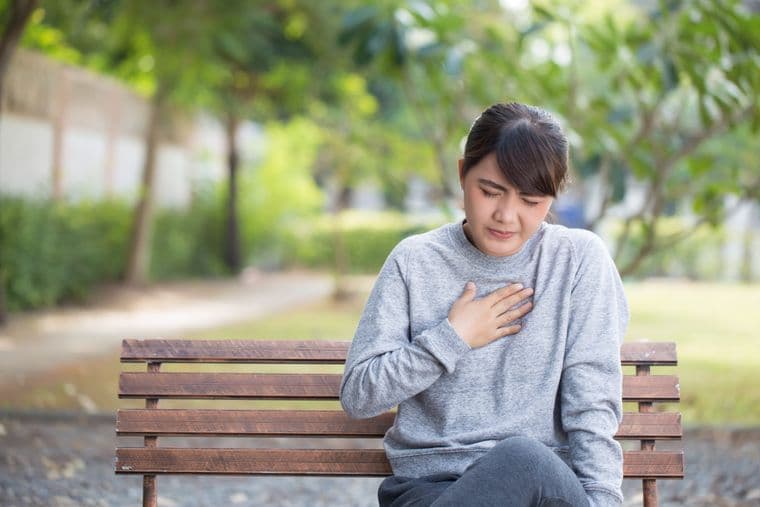 A woman, sat on a park bench, experiencing chest pain
