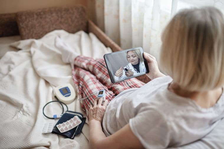 Woman in bed at home, looking at screen of laptop and consulting with a doctor