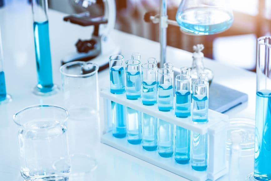 A laboratory scene with test tubes filled with blue liquid, a microscope, and other scientific equipment on a white surface.