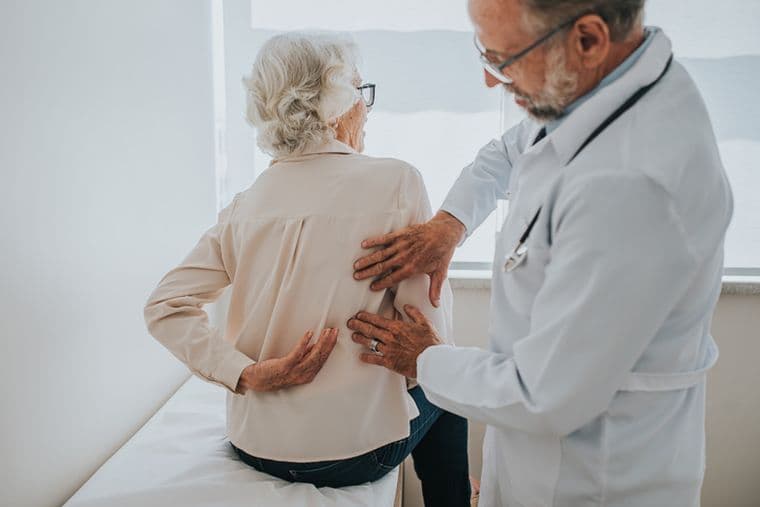 A doctor examines an elderly woman's back