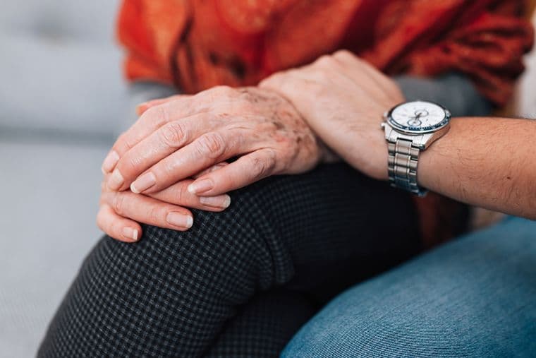A younger person offers comfort to an older person by holding their wrist