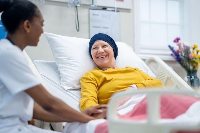 A female nurse of sits at the bedside of a smiling cancer patient