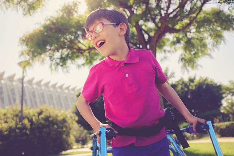A child with muscular dystrophy, using a walking frame, in a park